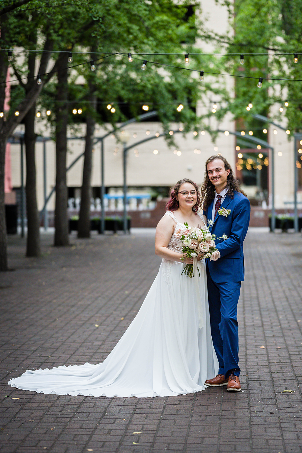 A bride in a white wedding dress and a groom in a bright blue suit stand in an alley in Downtown Roanoke for a photo together.