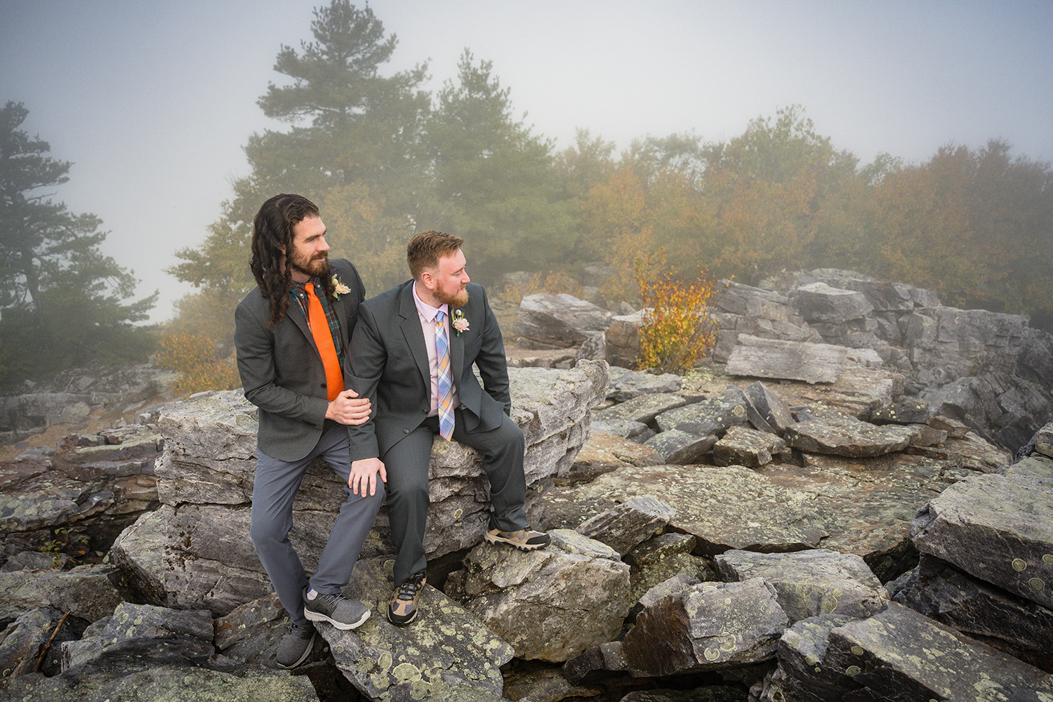 A queer couple sit together on a pile of rocks looking out at the foggy mountain views in Shenandoah National Park on their elopement day.