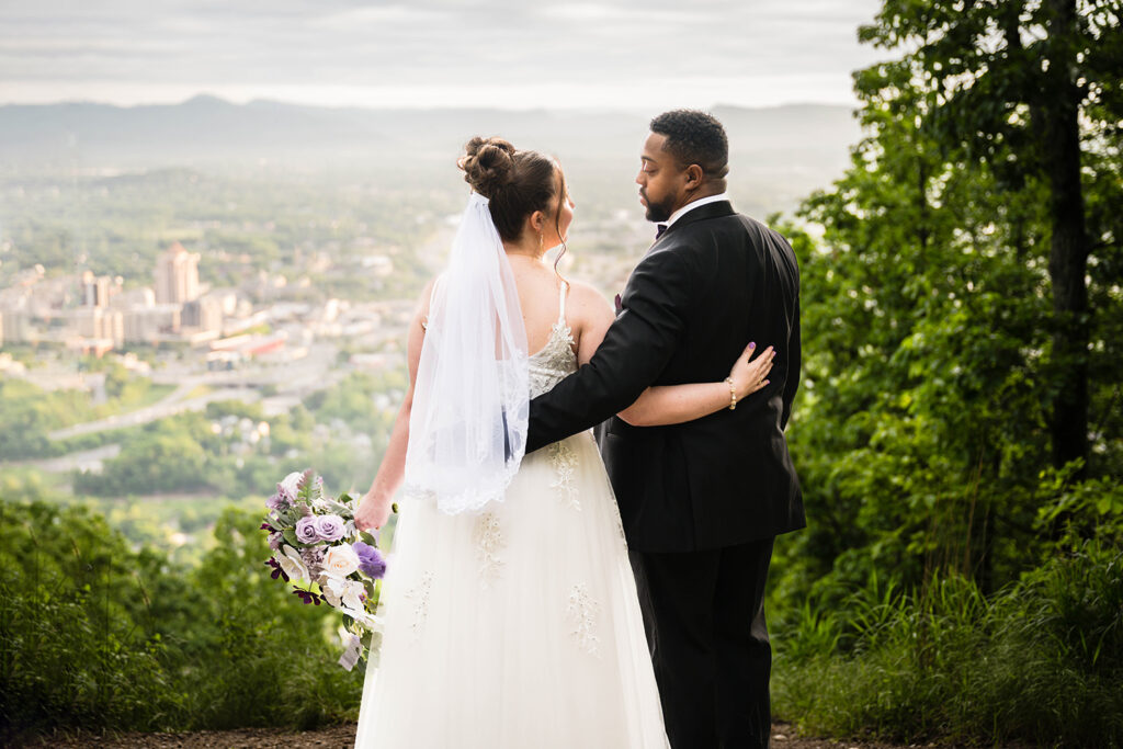 A couple looks at one another lovingly with the Roanoke skyline in the background.