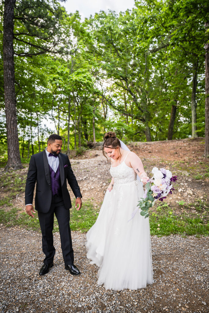 A man looks down at his partner's dress as she shows off the details of her dress to him.