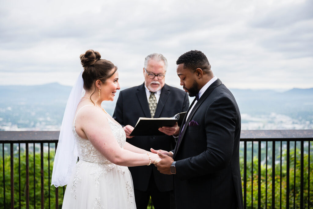 A couple on their elopement day stand in front of their officiant and hold hands. The man has his eyes closed and is getting emotional while the woman is smiling widely with tears forming in her eyes.