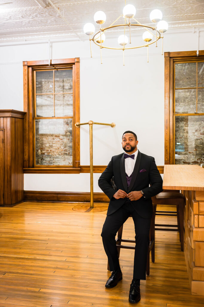 A man sits in a chair in a hotel lobby wearing a suit for his elopement day.