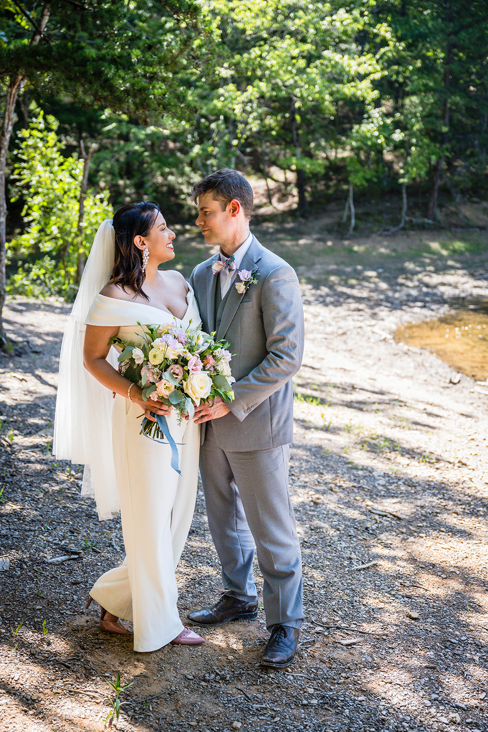 A couple on their elopement wedding day stand along the shores of Carvin's Cove and look at one another smiling in Roanoke, Virginia for a photo.