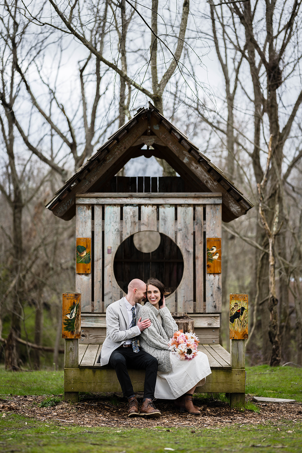 A couple sits and laughs together while sitting on a structure that resembles a bird house at Heritage Park in Blacksburg, Virginia on their elopement wedding day.