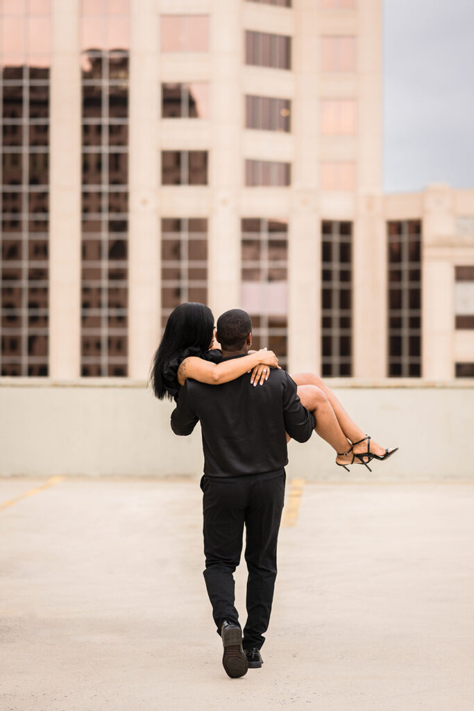 A Black man carries his fiancée for their parking garage engagement photos in Roanoke, Virginia.