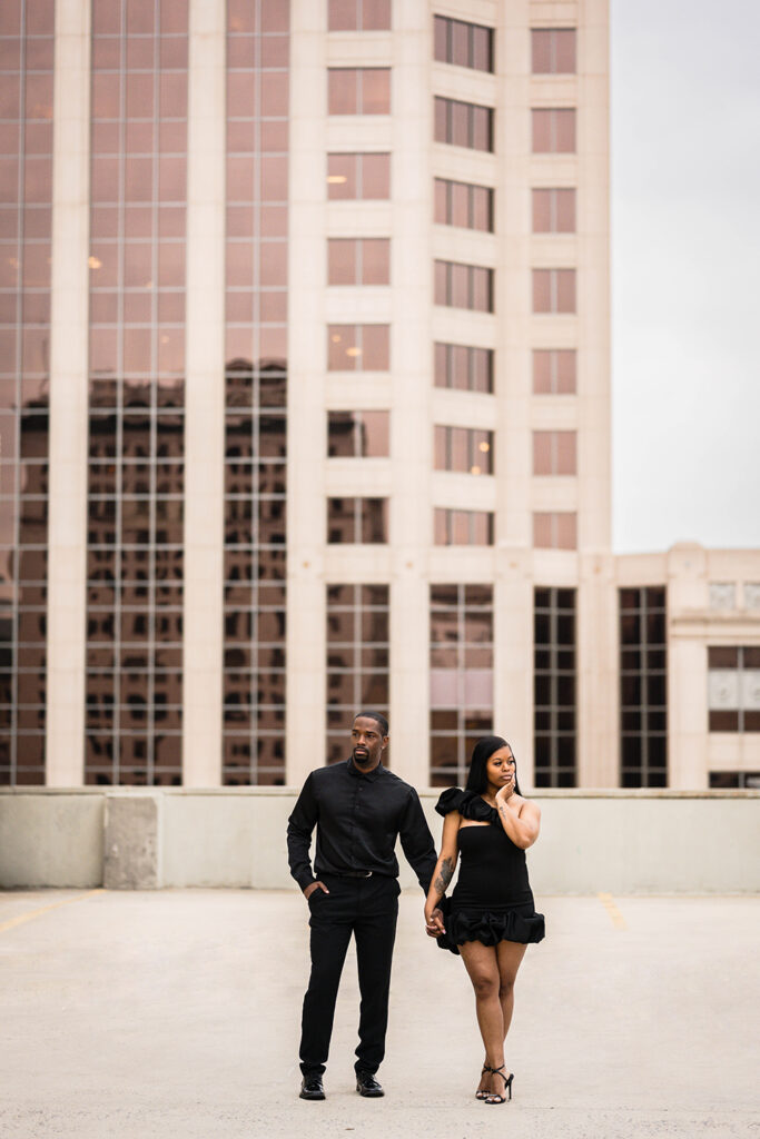 A Black couple hold hands and look stoic and serious for their parking garage engagement photos in Roanoke.