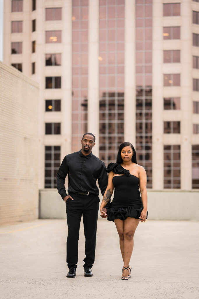 A Black couple hold hands and look stoic and serious for their parking garage engagement photos in Roanoke.