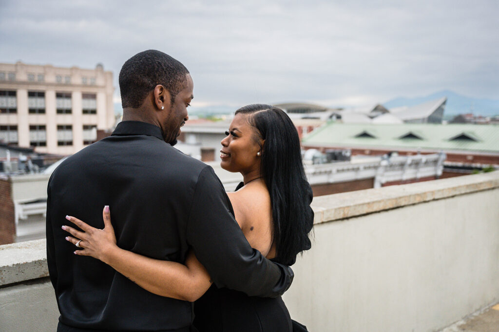 A Black couple looks at one another and smiles on the top of the Center in the Square parking garage in Roanoke, Virginia.