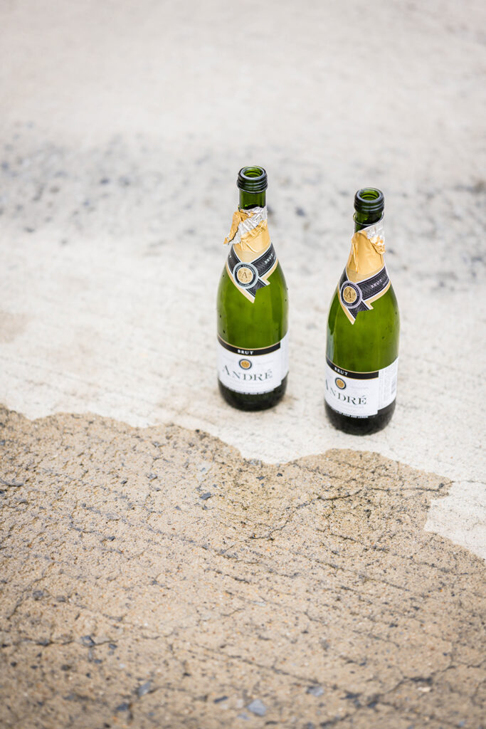 Two open bottles of champagne are placed on the ground next to a puddle of champagne.