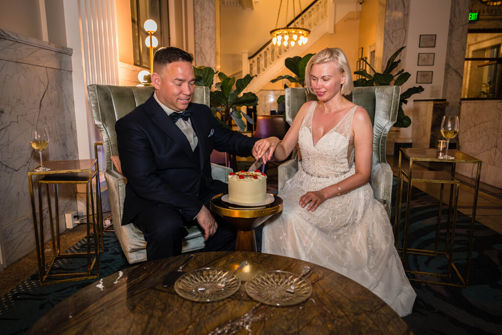 A couple sits in the lobby of the Liberty Trust Hotel and cuts into their wedding cake.