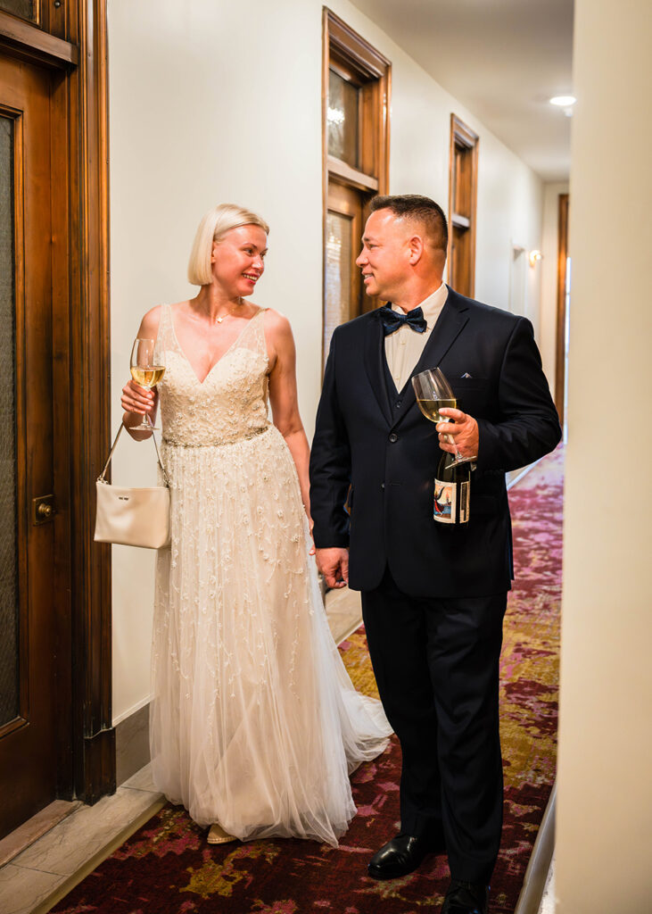 A couple walk hand-in-hand down the hallway to get to their room at the Liberty Trust hotel in Roanoke, Virginia. Each of them holds a glass full of wine in the other hand.
