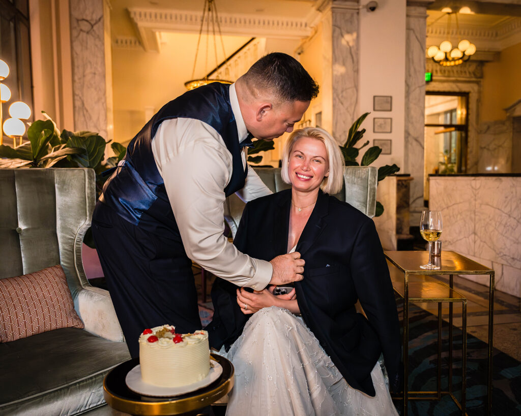 A groom takes off his suit jacket and gives it to his cold bride during their elopement day. The two are inside of the Liberty Trust Hotel in Roanoke, Virginia.