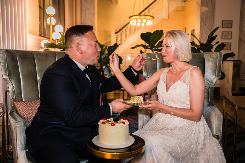 A couple feeds one another a piece of wedding cake while sitting in the lobby of the Liberty Trust Hotel in Roanoke, Virginia.