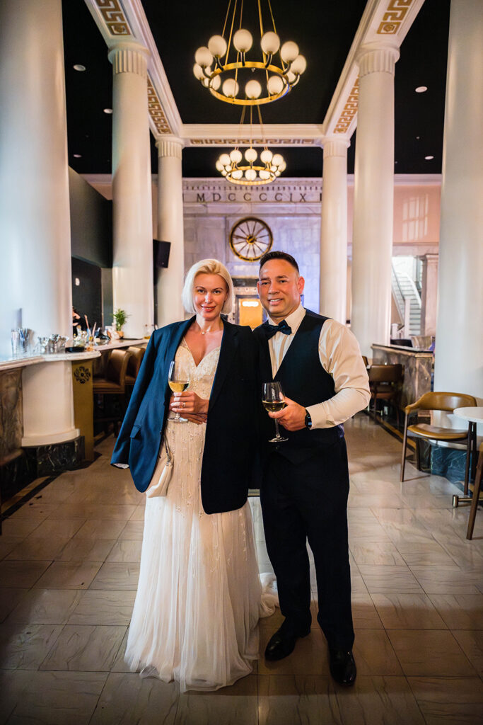 A couple stands together and smiles for a photo inside of the Liberty Trust hotel's lobby on their elopement day.
