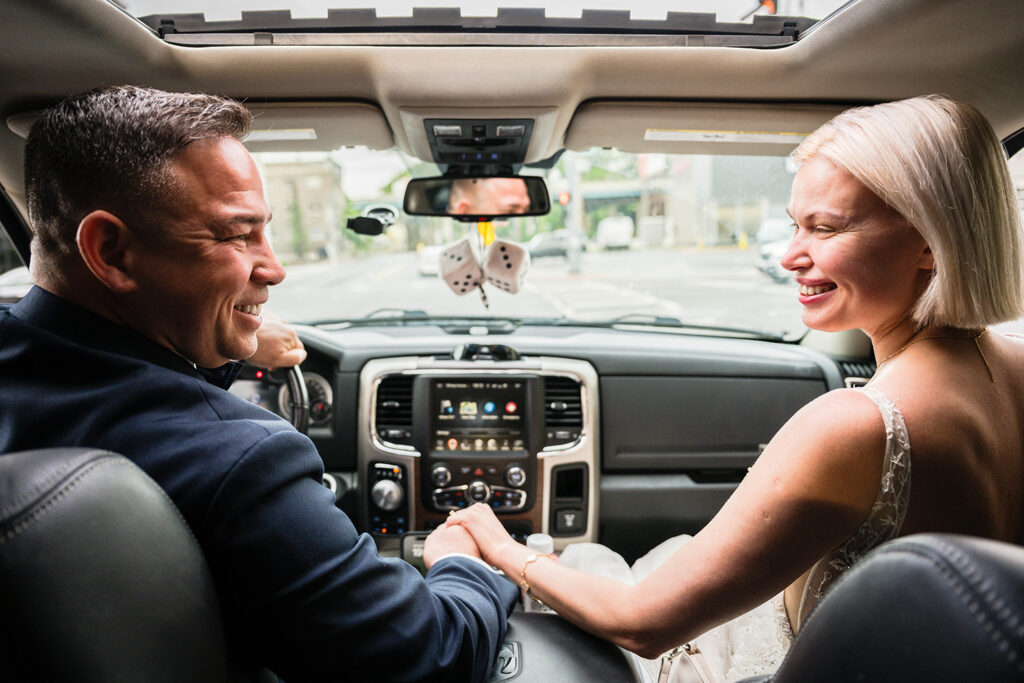 A couple smiles and holds each other's hands for a brief moment in the car on their wedding day.