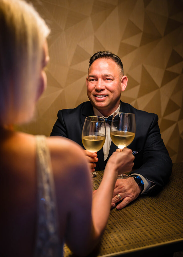 A man holds a wine glass to his partner and smiles.