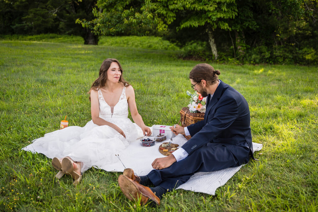 An elopement couple sit on a blanket for a light dinner picnic at Cahas Mountain Overlook.