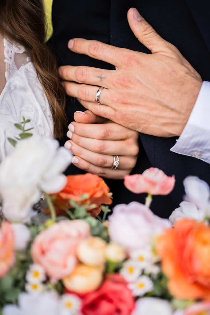 A close up shot of wedding rings on the couple's hands, slightly in the background of the bride's bouquet.