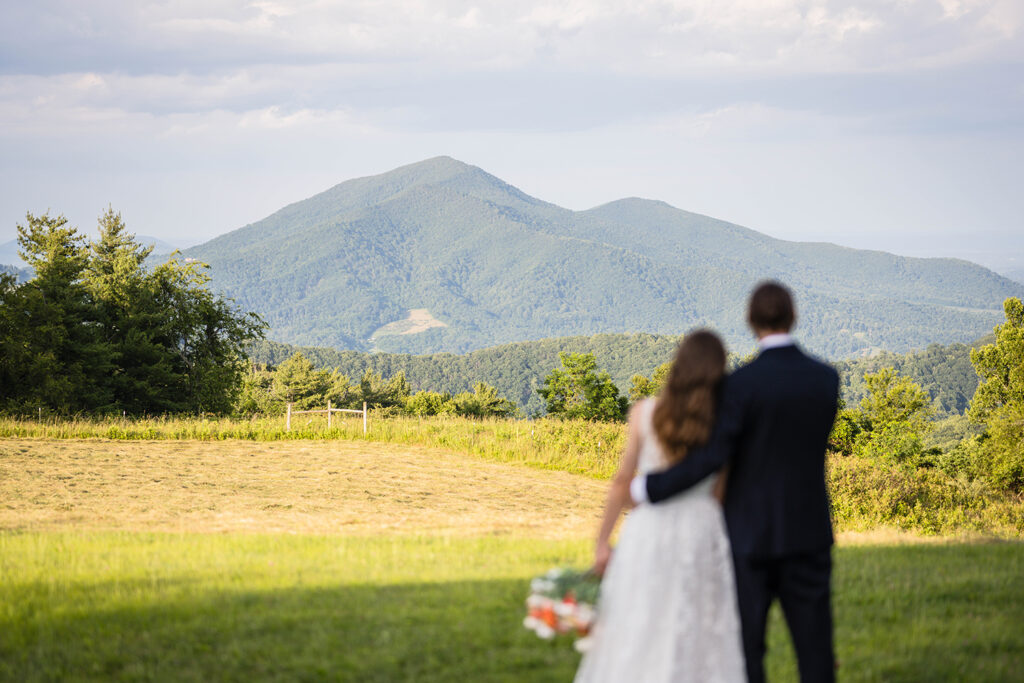 A blurred man and woman embrace one another as they look towards Cahas Mountain, which is in focus, during their Blue Ridge mountain wedding day.