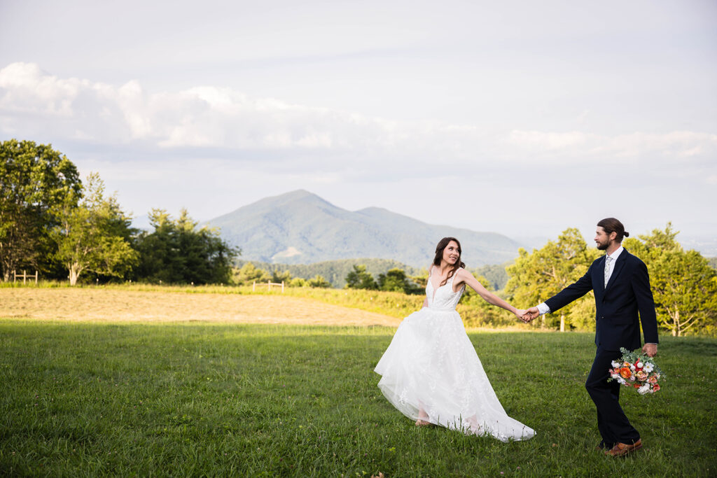 A wedding couple walk hand-in-hand and smile during golden hour at an overlook in the Blue Ridge Mountains.