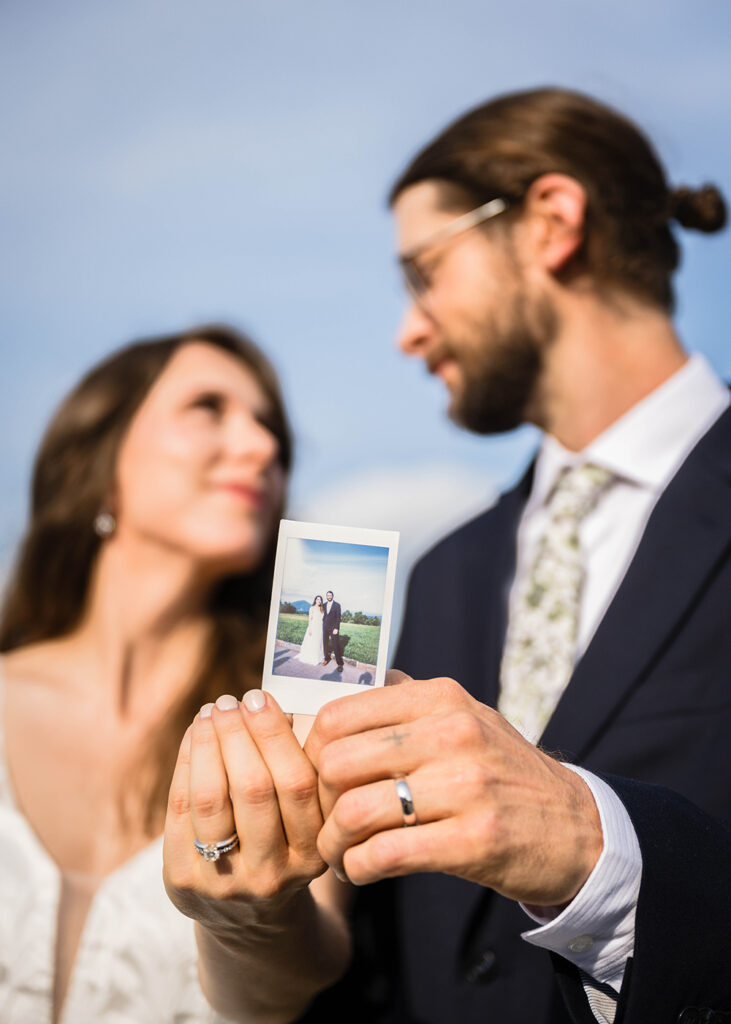 An elopement couple look at one another as they hold out a Polaroid photo of them taken by their friend on their Blue Ridge Parkway wedding day.