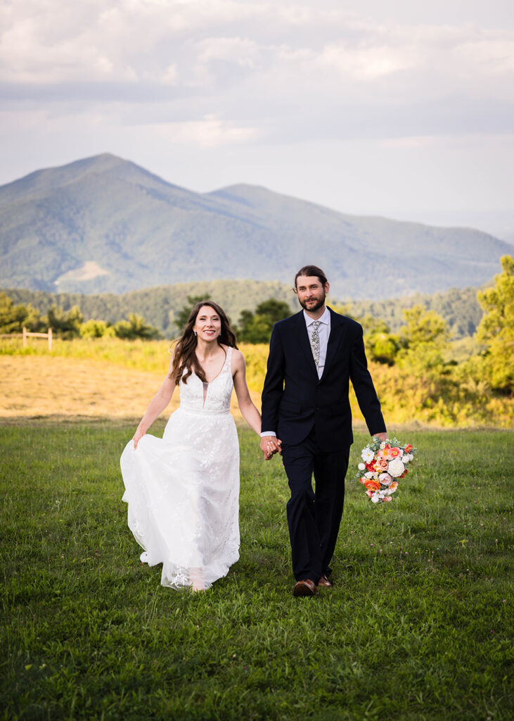 A wedding couple walk hand-in-hand and smile during golden hour at an overlook along the Blue Ridge Parkway.