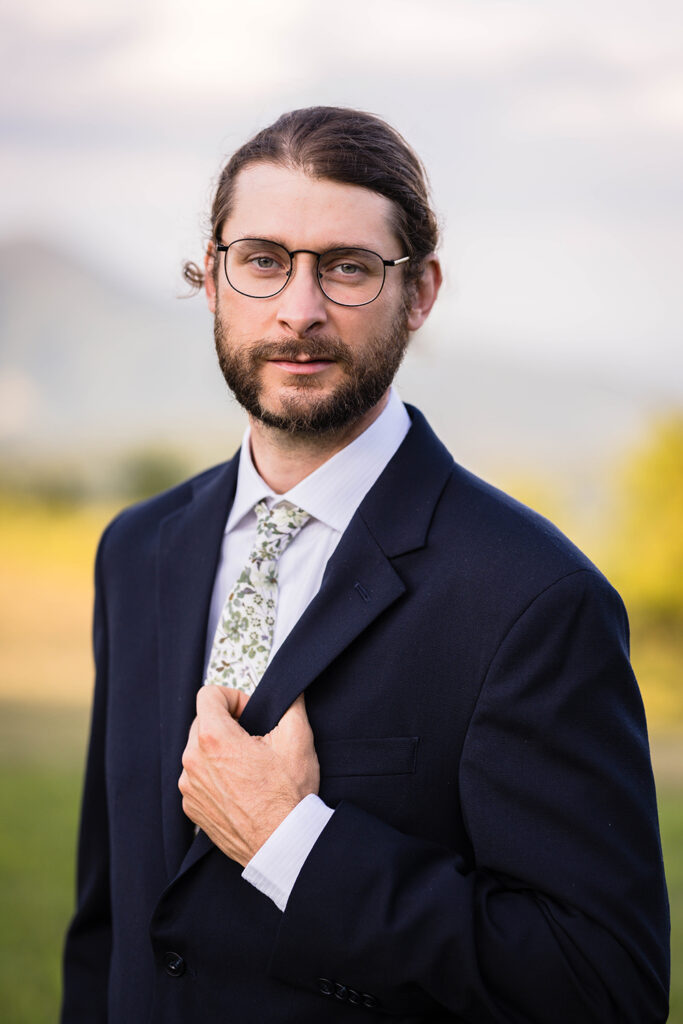 A man wearing a navy blue suit and a floral tie poses in front of Cahas Mountain for golden hour Blue Ridge Parkway wedding portraits.