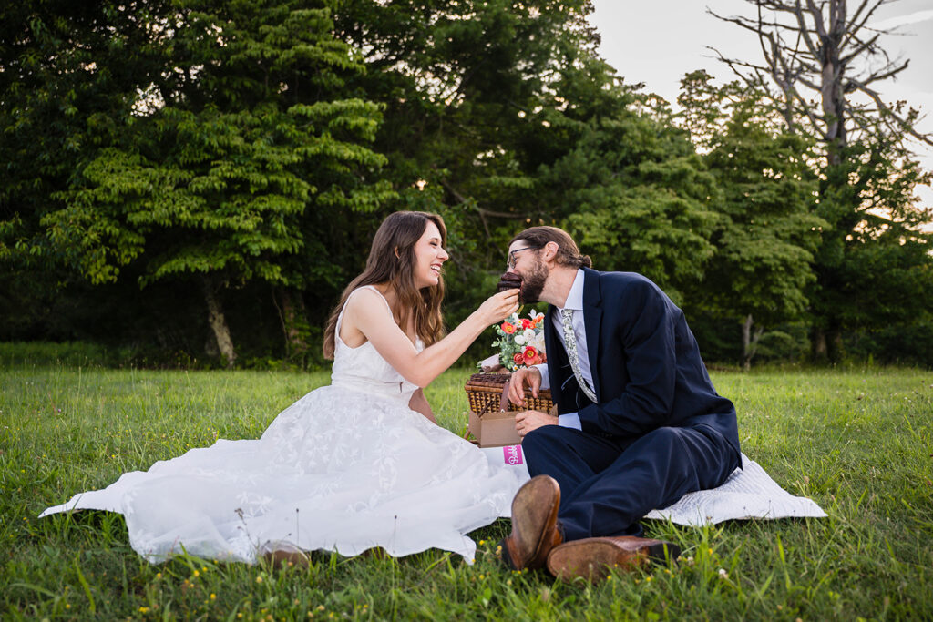 A marrier feeds her partner a cupcake and begins to smile widely as he takes an enormous bite.