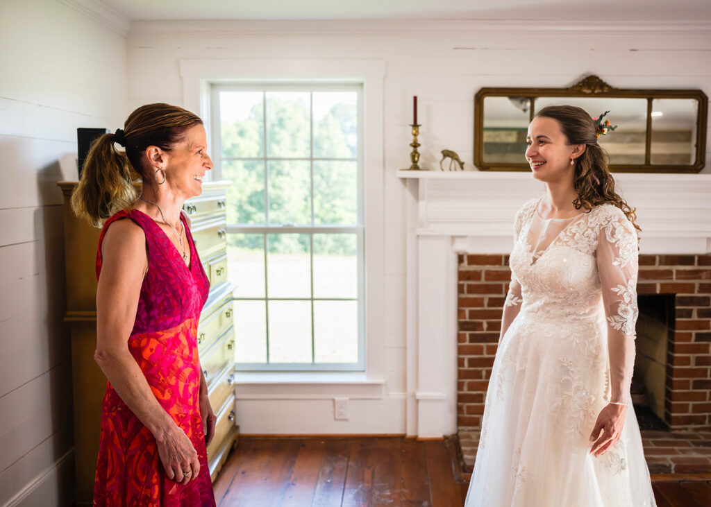 The mother of the bride smiles softly as the bride turns to show herself in her gown.