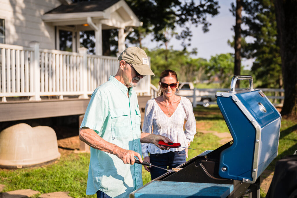 Two people stand in front of an open grill in the summer grilling turkey burgers.