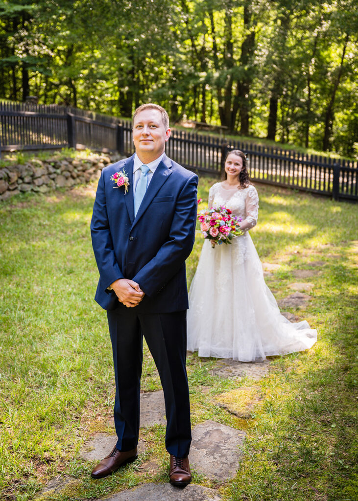 A marrier in a wedding suit smiles softly as he waits to be told to turn around to face his partner during a wedding day first look.