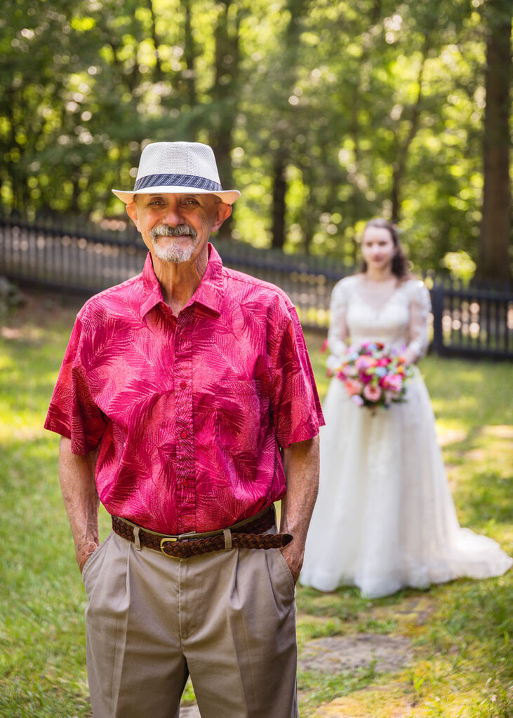 The father of the bride smiles softly as he waits to be told to turn around to face his daughter during a wedding day first look.