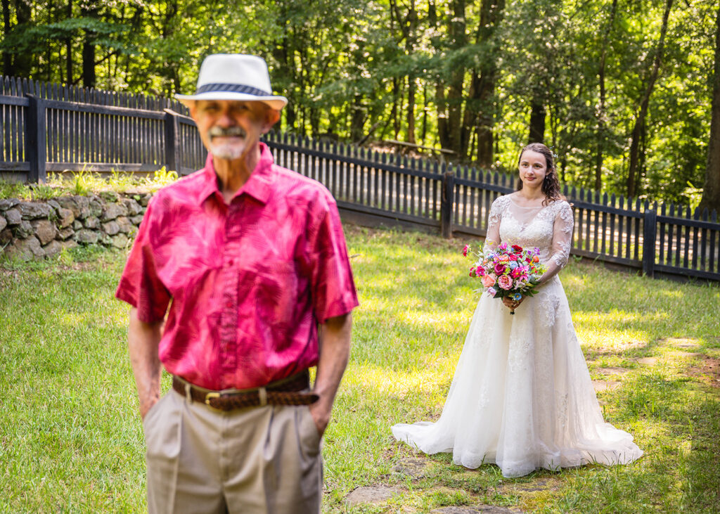 A marrier in a wedding dress waits patiently for her Dad to turn around during their first look.