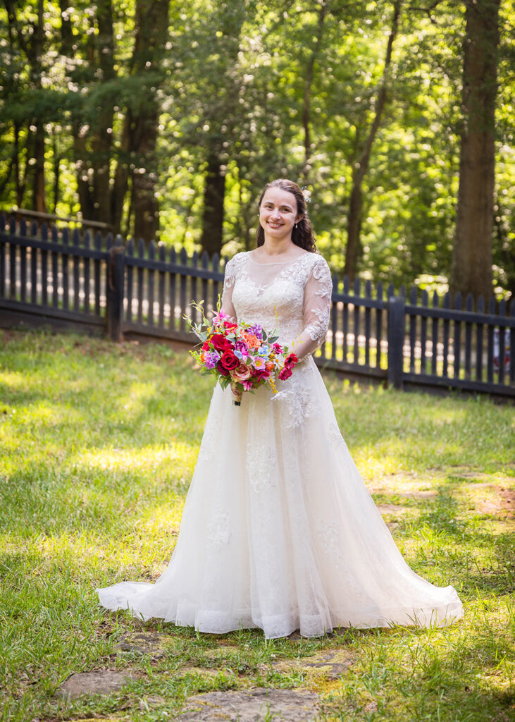 A bride wearing a vintage wedding dress and holding a colorful and vibrant bouquet smiles widely as she's set up for first looks on her Martinsville, Virginia elopement day.