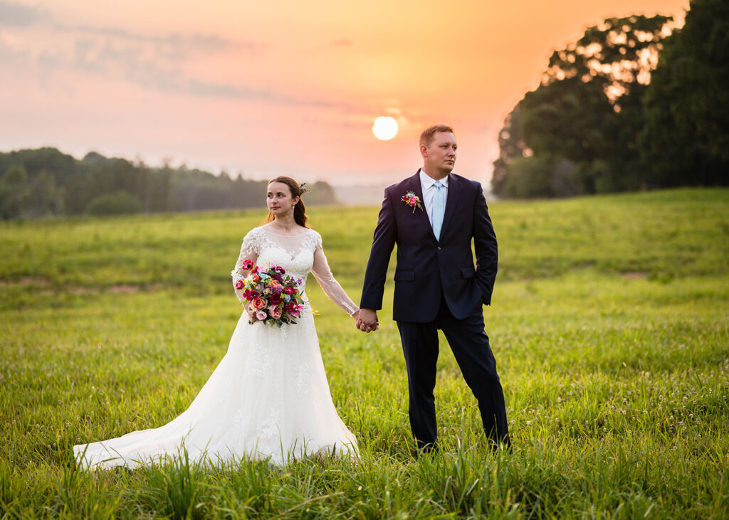 A couple holds hands in front of a golden sunset. Each person looks off in opposite directions for a stoic and dramatic photo.