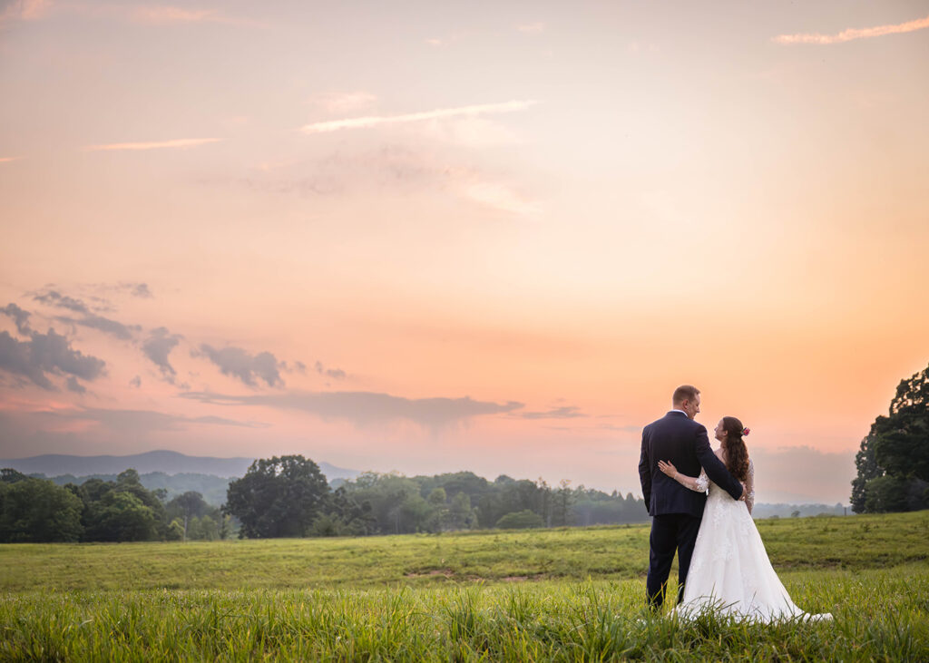 A wedding couple wrap their arms around one another and exchange a look at one another as the sun dips below the horizon.