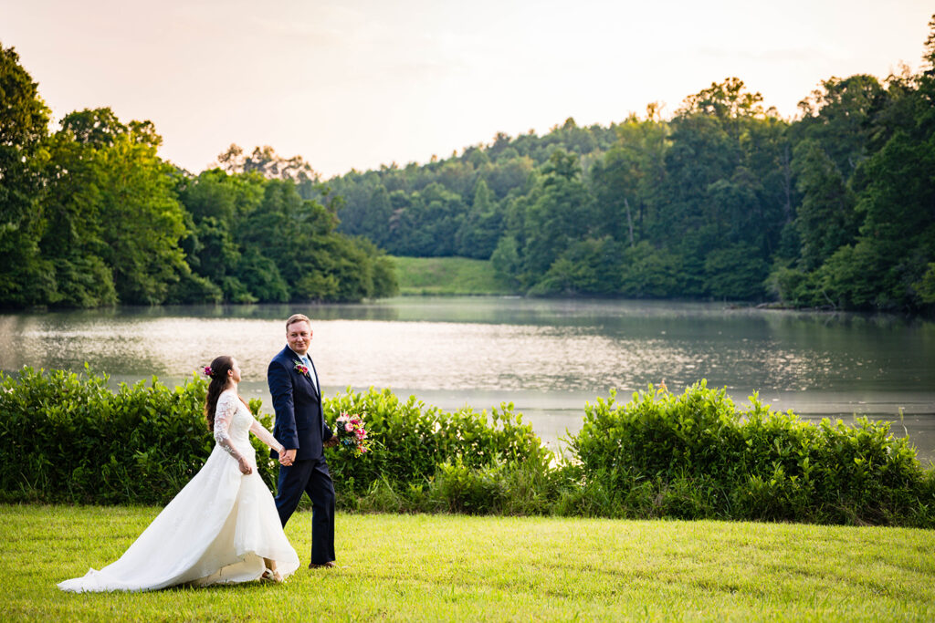 An elopement couple walk hand-in-hand in front of a pond at golden hour during their Martinsville, Virginia wedding.