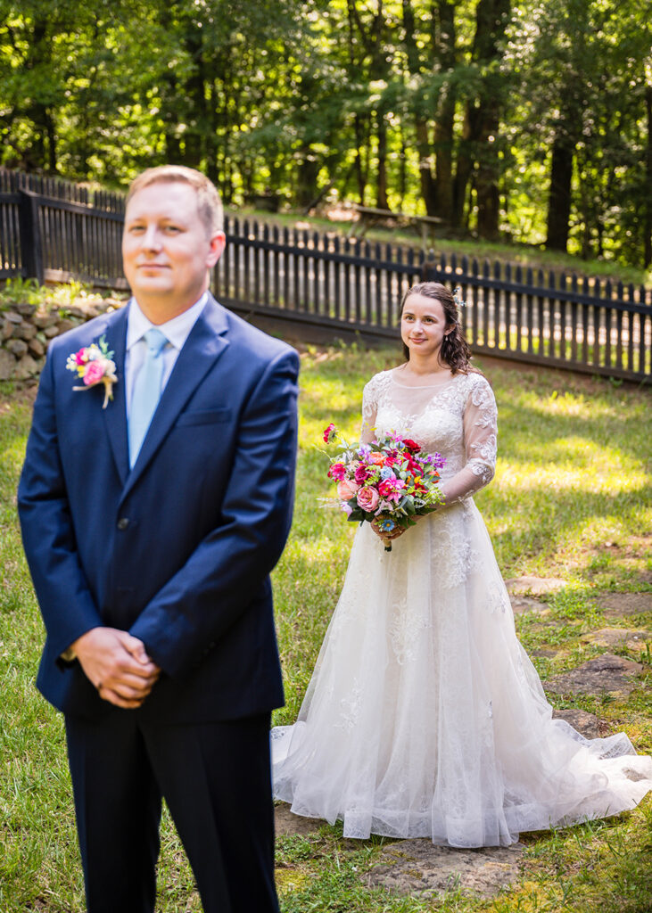 A marrier in a wedding dress waits patiently for her partner to turn around during their first look.
