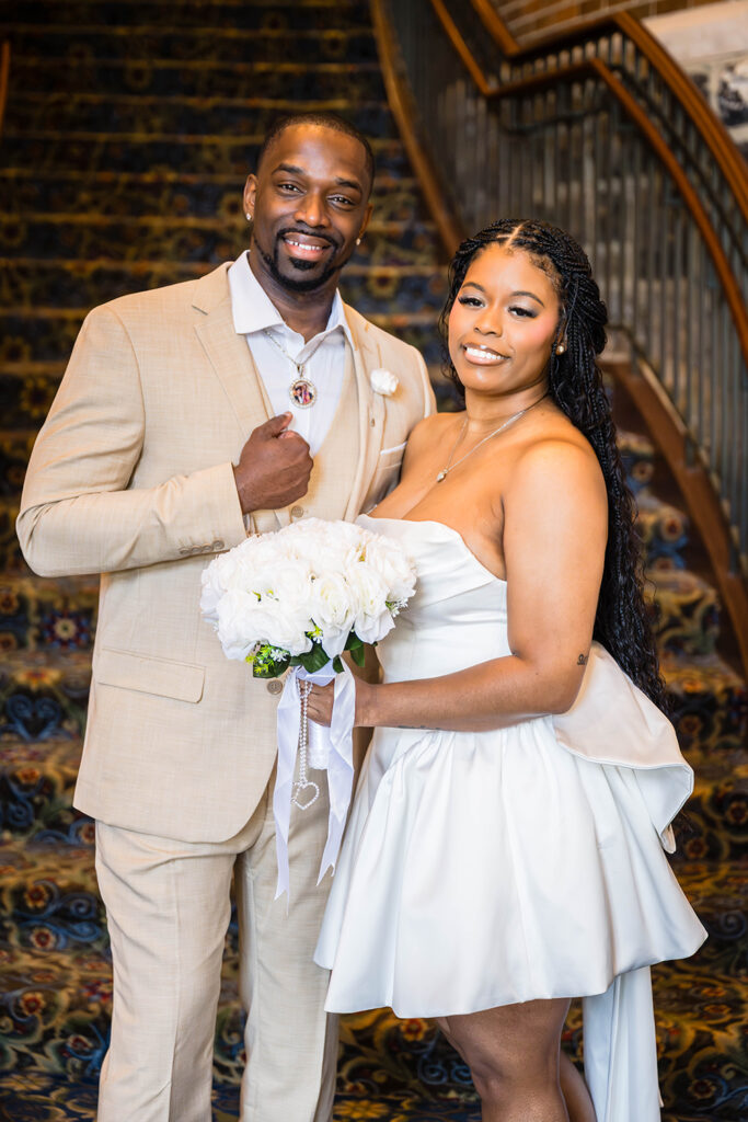 A wedding couple pose for a photo together at the base of the grand staircase in Hotel Roanoke. The pair smile towards the camera.