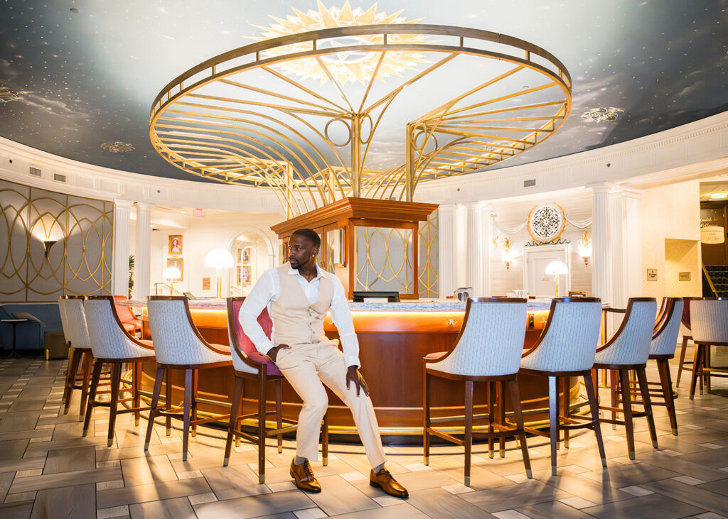 A Black man wearing a tan suit poses in the Hotel Roanoke lobby bar while getting ready for his Downtown Roanoke wedding.