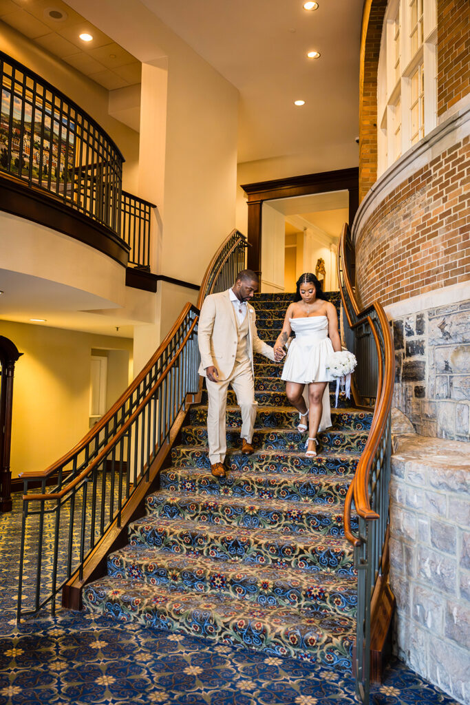 A Black wedding couple walk down the stairs of the grand staircase in Hotel Roanoke.