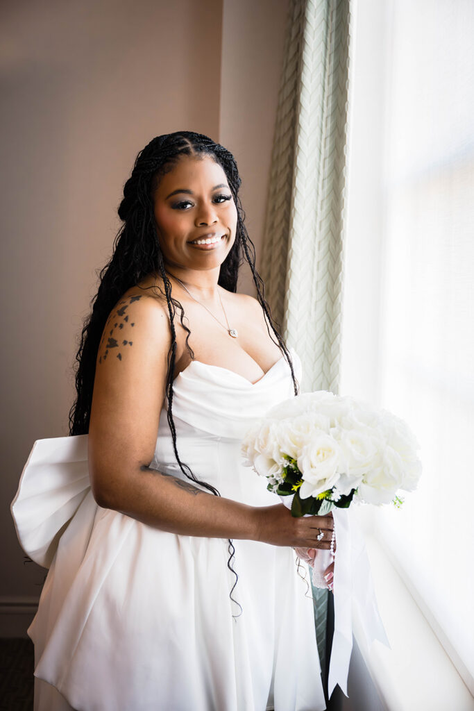 A marrier wearing a strapless wedding dress smiles for a photo as she holds a bouquet of flowers.