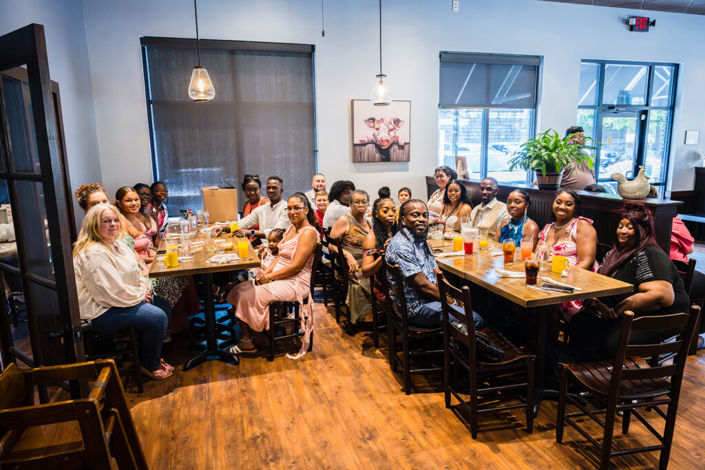 A group of twenty two people are seated in a restaurant. The group looks up for a photo.