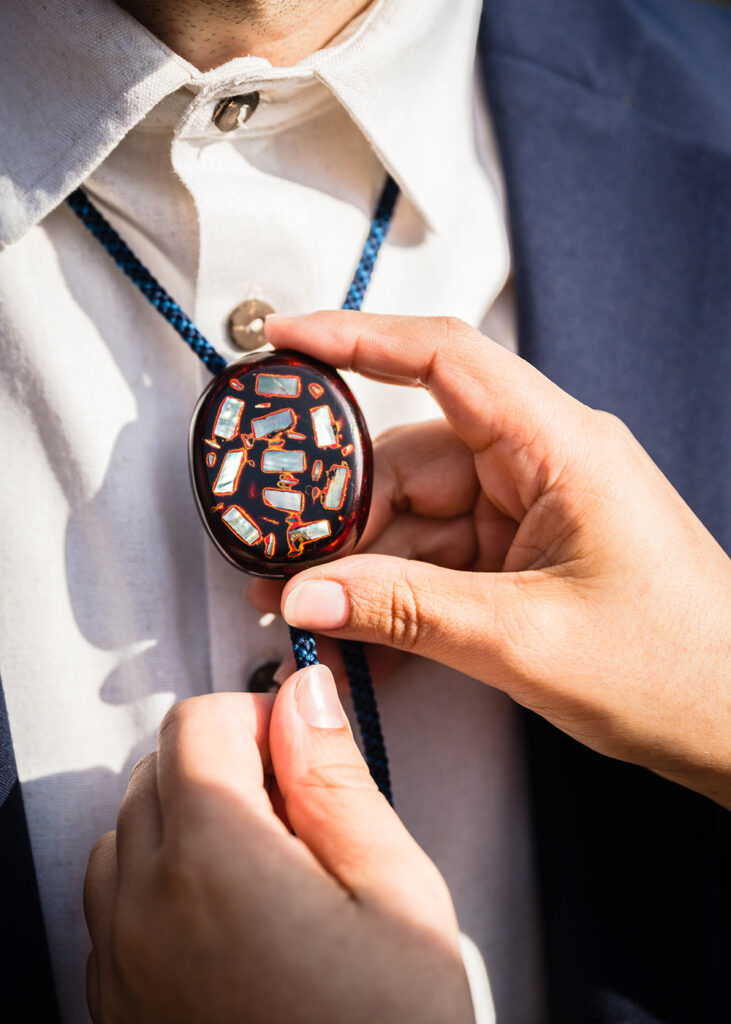 A close up photo of two hands adjusting a bolo tie.