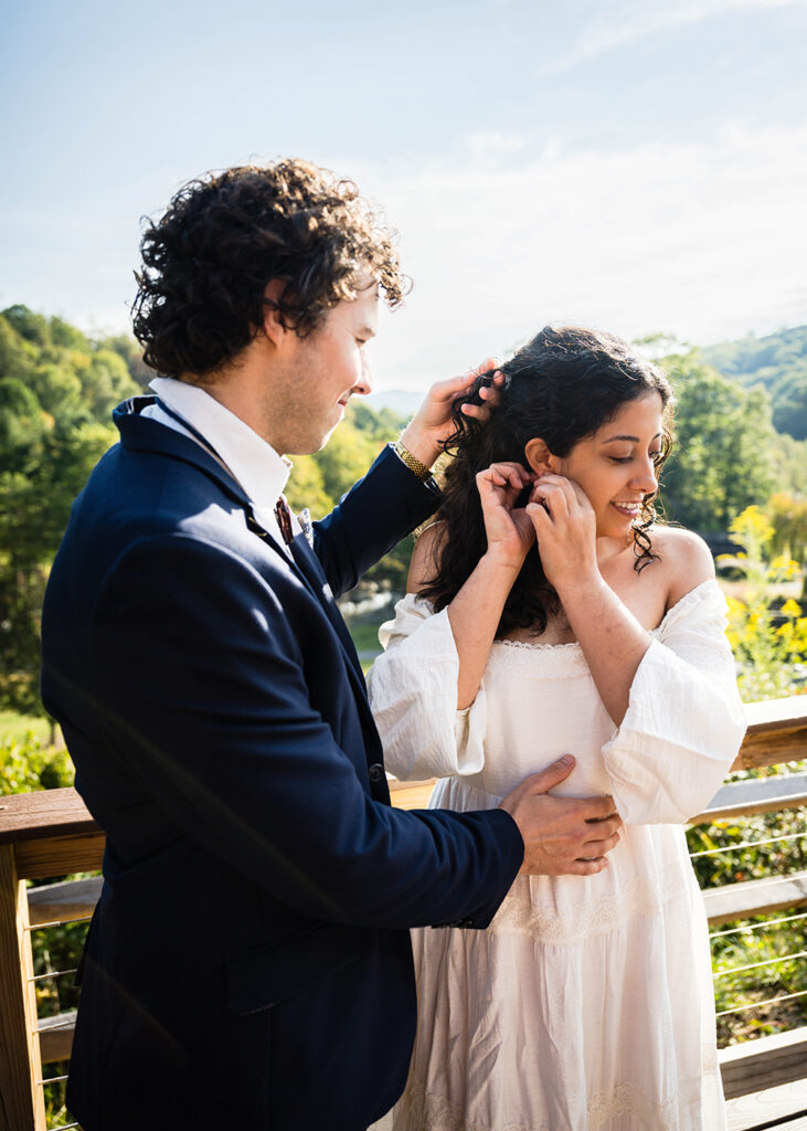 A man moves a strand of hair from his partner's face to help her put a earring in on their wedding day.