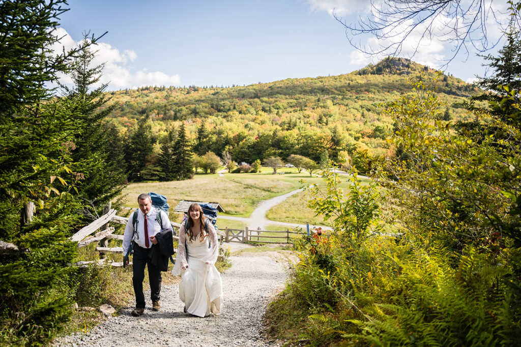 An elopement couple start their Massie Gap trail hike. They're wearing their wedding attire and have on big hiking backpacks.