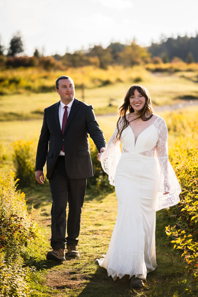 A bride wearing a wedding dress leads her partner down a path in between wildflowers at Grayson Highlands State Park.