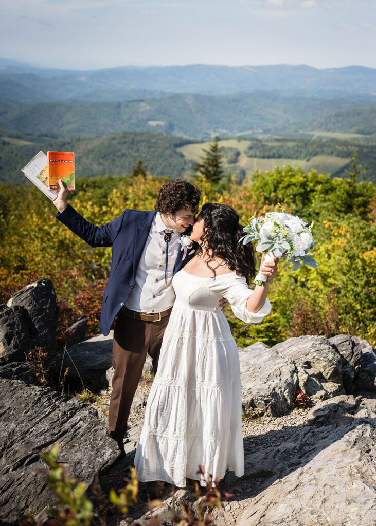 A man holds up two books as he goes in to kiss a woman holding up a flower bouquet.