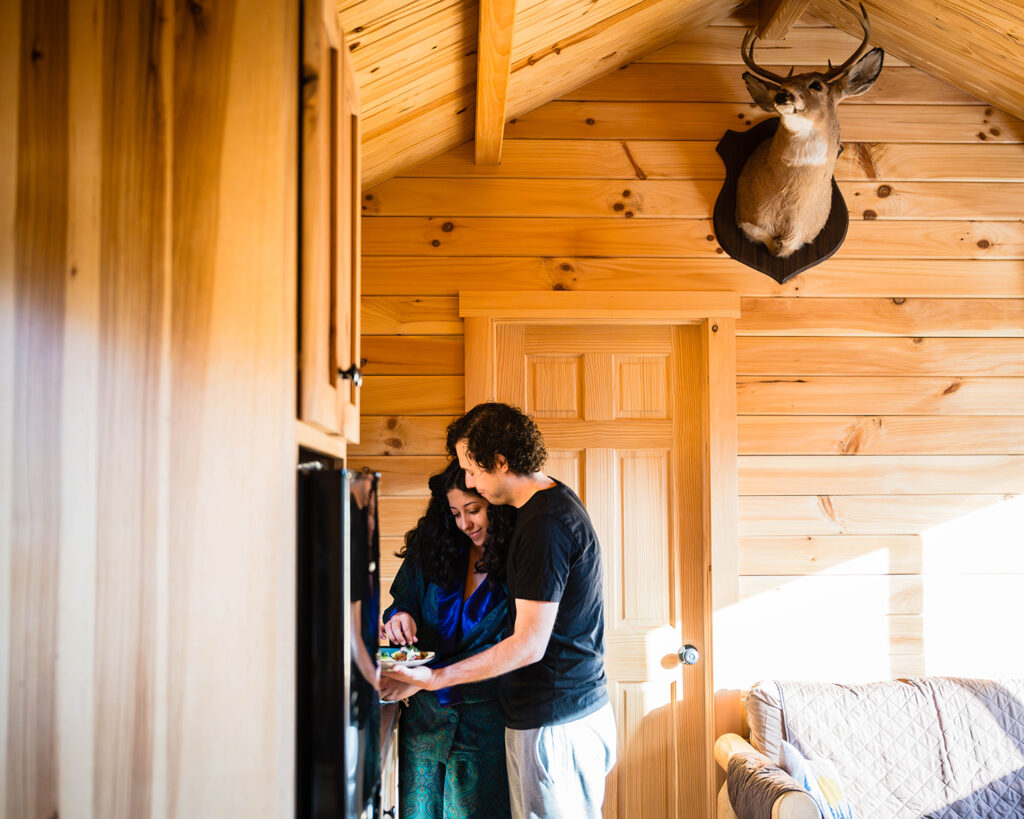 A couple embraces as they prepare plates of food for themselves inside of The Overlook Airbnb at Highland Hideaways.