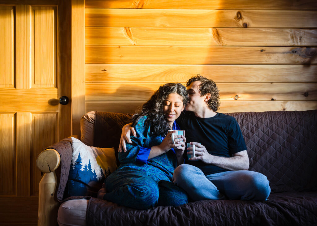 A couple snuggles up on the couch in their Airbnb, each with a coffee cup in hand.